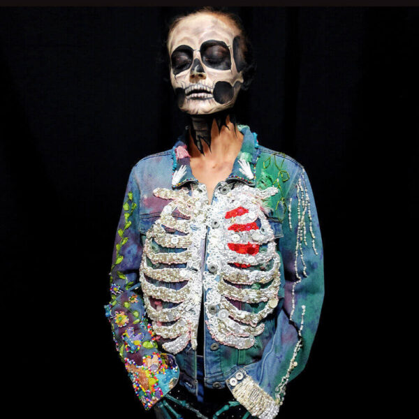 Dua Tua wearing the "Bones Jacket" against a black background, her face intricately painted by BIMANA FX to resemble a skull.