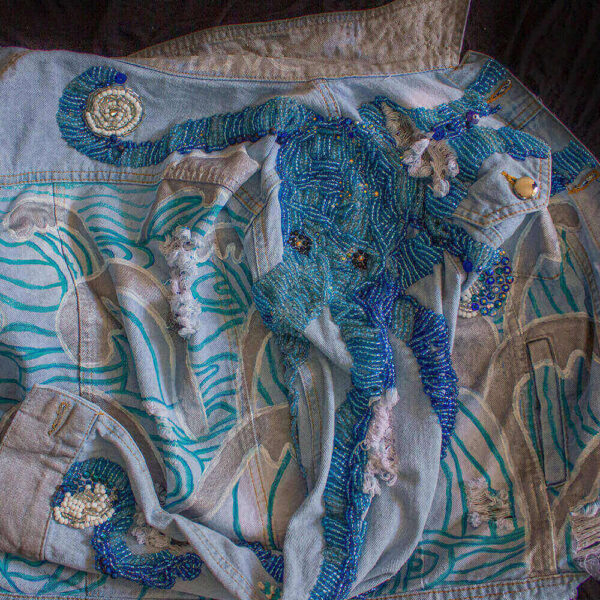 Detail of one of the Pulpis denim jackets showcasing the embroidered beaded octopus at the back with tentacles in shades of blue and light blue. The piece also features painted wave textures