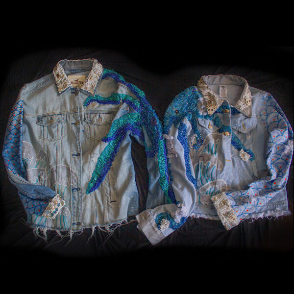 Front view of the 'Pulpis' denim jacket pair, featuring decorative embroidered beaded tentacles in various shades of blue on the shoulders and arms of the jackets. The jackets also showcase decorative embroidery with white beads on the collar and cuffs, along with hand-painted ocean waves