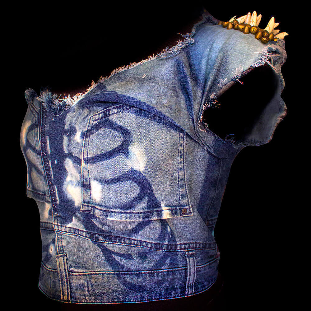 Left side view of the Denim Bony Blouse, showcasing the intricate decorations on the left shoulder, where the marble spike rivets and golden-brown beads are beautifully embroidered. The front of the blouse reveals a stunning painted ribs pattern created through a bleach tie-dye process