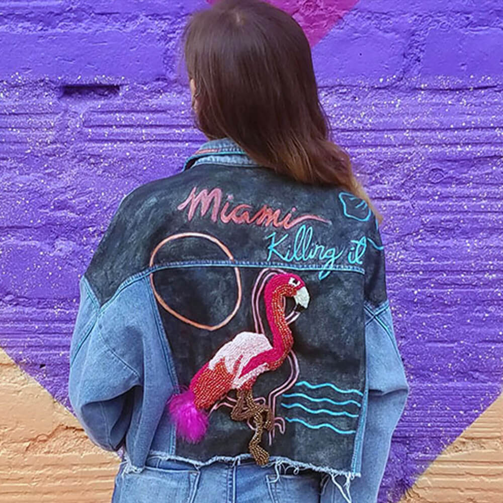 Model with her back to the camera, displaying the "Miami Vice" jacket featuring a flamingo bead patch on the back.