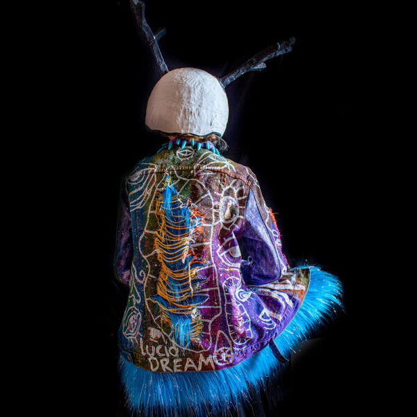 Model sitting with her back turned, showcasing the Alien denim jacket and its ripped effect on the back