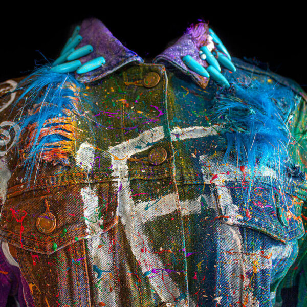 Close-up detail of the collar of the Alien denim jacket with sewn turquoise spike beads around the neck, hand-painted letters on the jacket, and paint splatters on the fabric