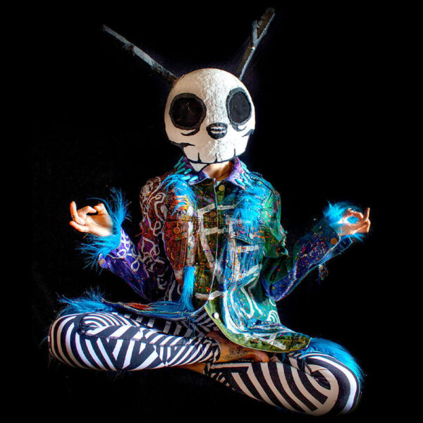 The model is seated in a meditative position, wearing the Alien denim jacket along with the Dua Tua skull mask. The jacket features furry textiles