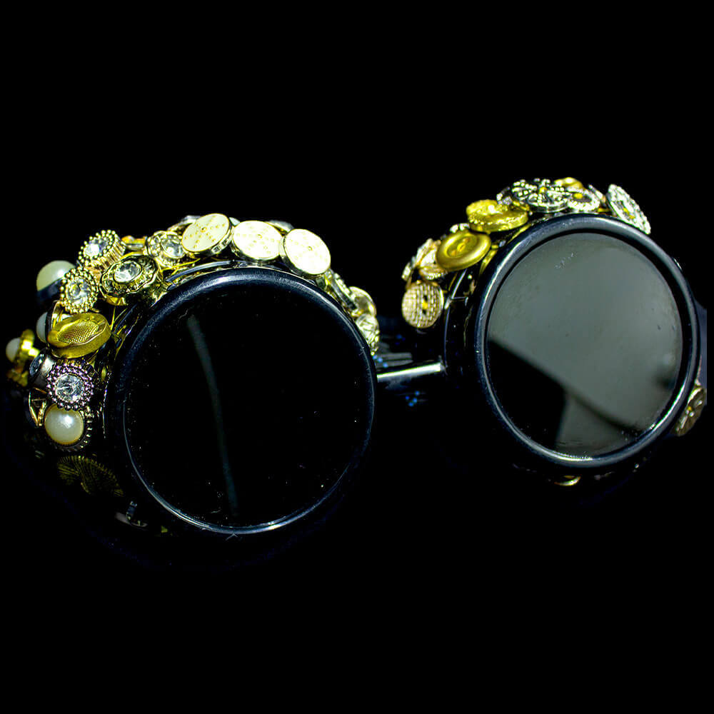 Front view of the golden goggles. The goggles are black with a texture of golden buttons on the top of the frames