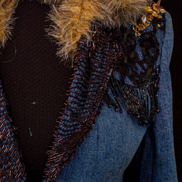 Close-up of the front lapel of the She Fox denim jacket with copper pipe beads and black flower lace decorations at the shoulder