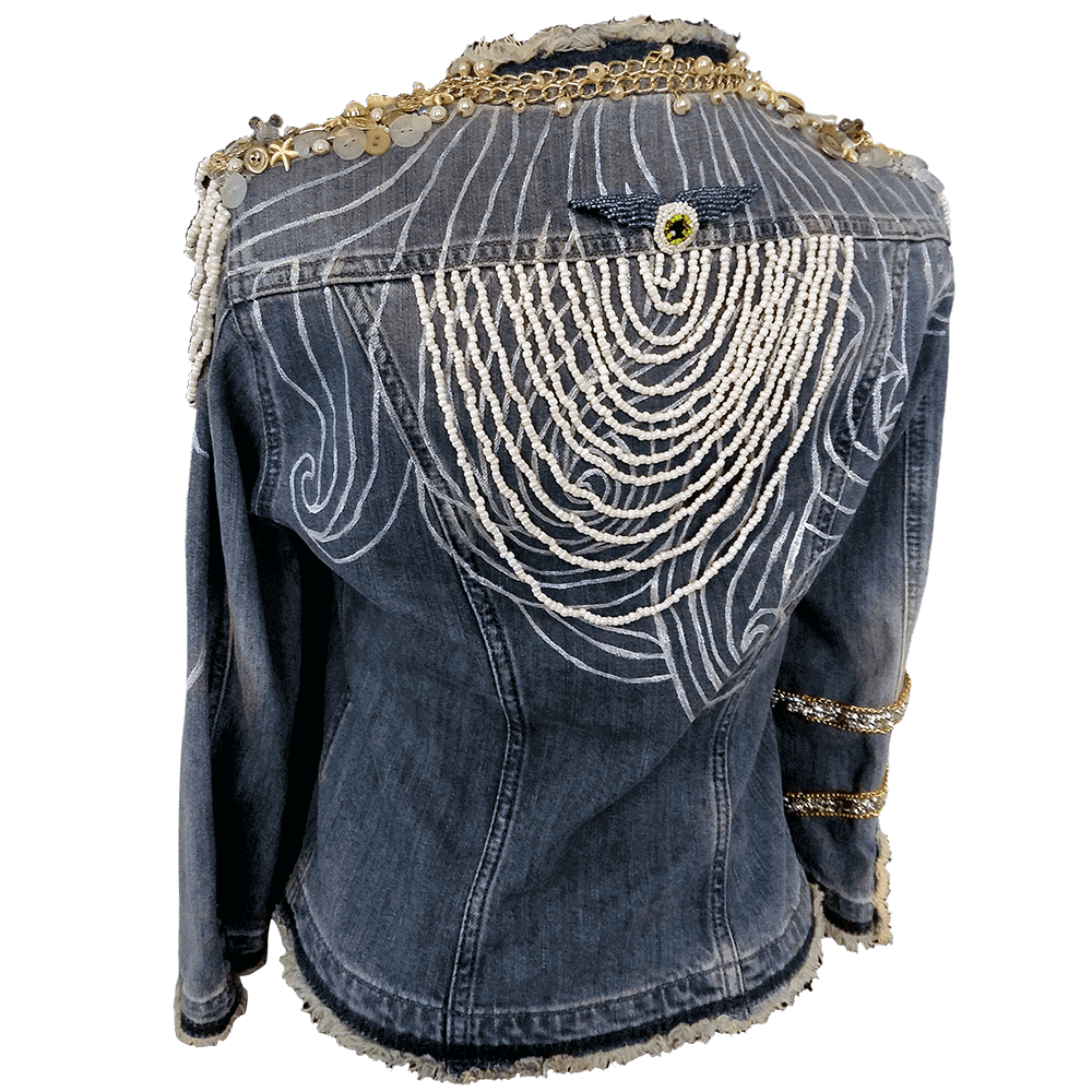 Back view of the Windy Jacket in denim with white bead decoration on the back. The jacket features a painted texture with white paint in lines, a removable beaded patch, white and transparent buttons on the shoulders, pearl and white beads, and golden chain decorations encircling the jacket's collar