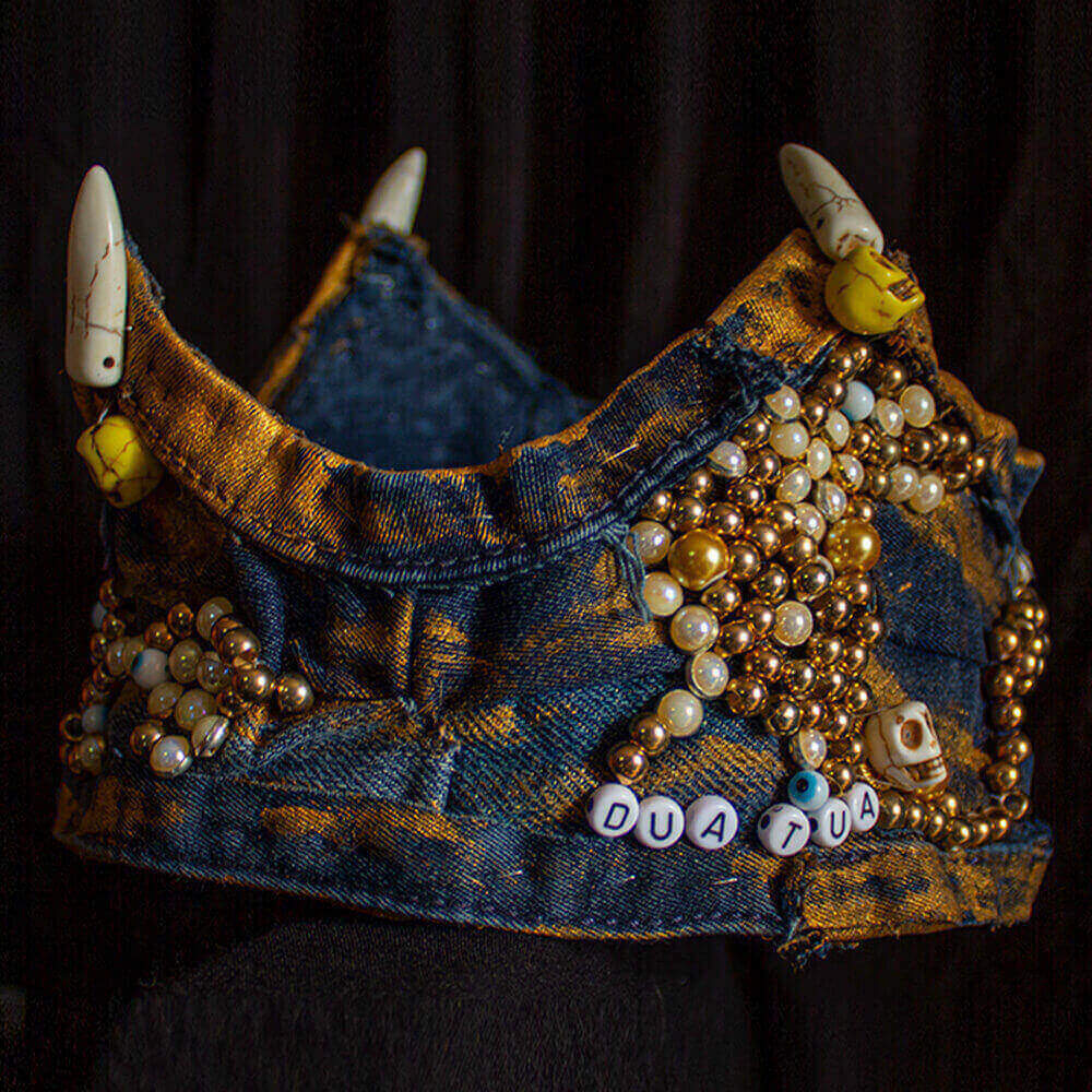 Side view of the Queen denim crown made with recycled jean fabric decorated with gold fabric paint, fake pearls beads, fake gold beads, letters rounded beads, skulls and spikes embroidered accessories