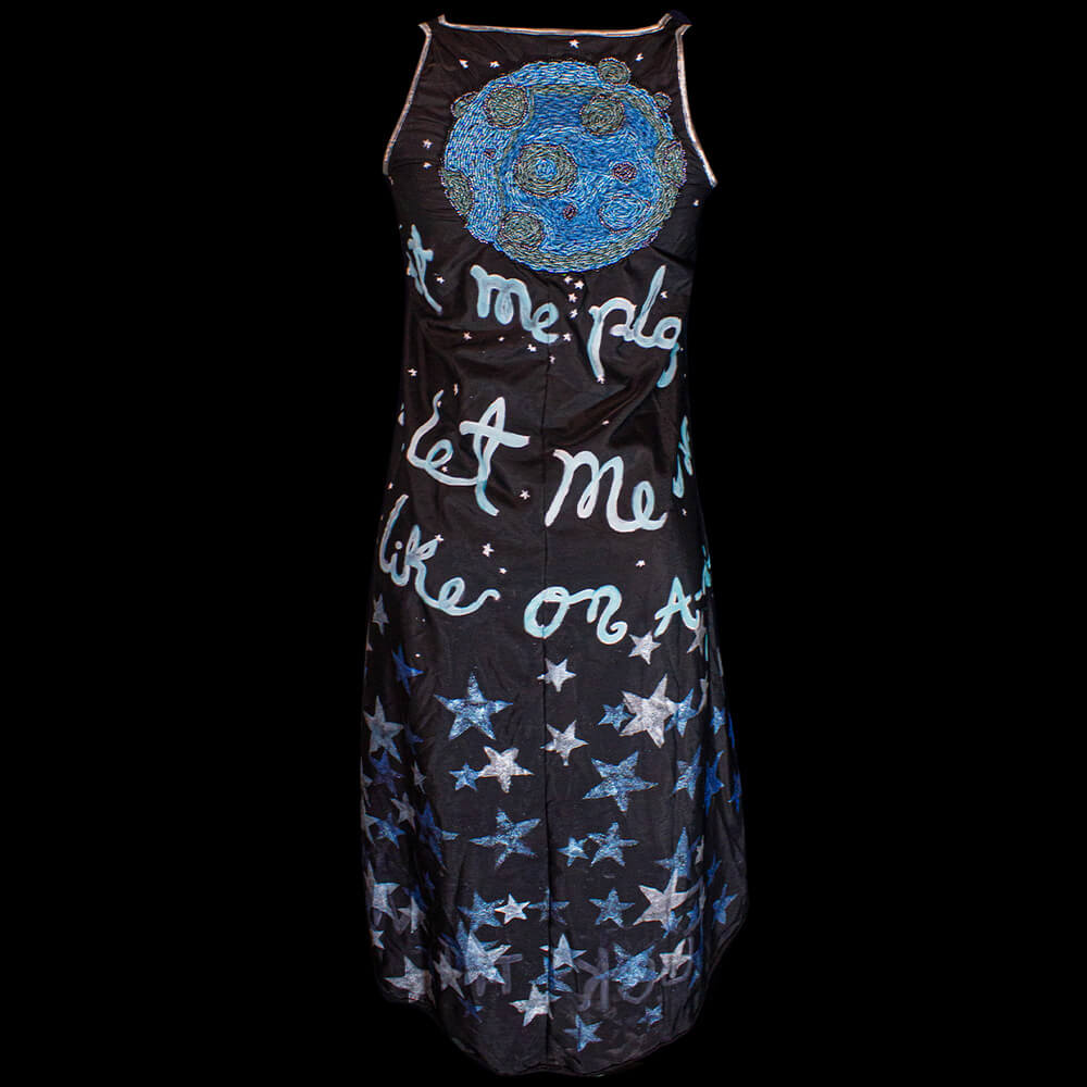 Back view of the Fly me to the Moon polyester black dress with an embroidered moon on the upper back and decorated with fabric paint all over the drees with texts and stars