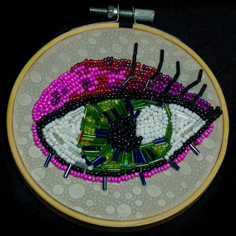 Front view of the Green Eye frame embroidered with vibrant hues of fuchsia, green, and white beads