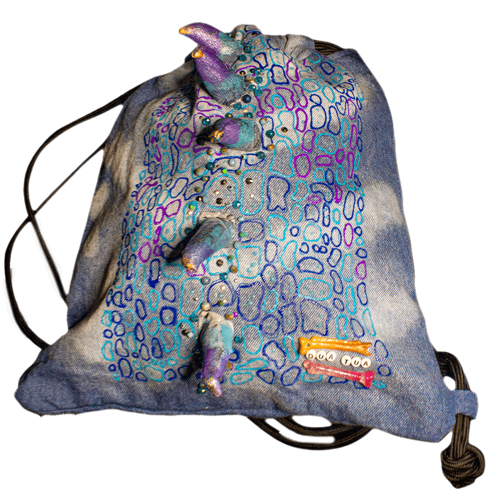 Front general view of the Blue Iguana denim drawstring decorated with a crest made of denim scraps, embroidered decorative beads, 3D paint, resin bones accessories, letter beads, bleach denim effect and fabric paint