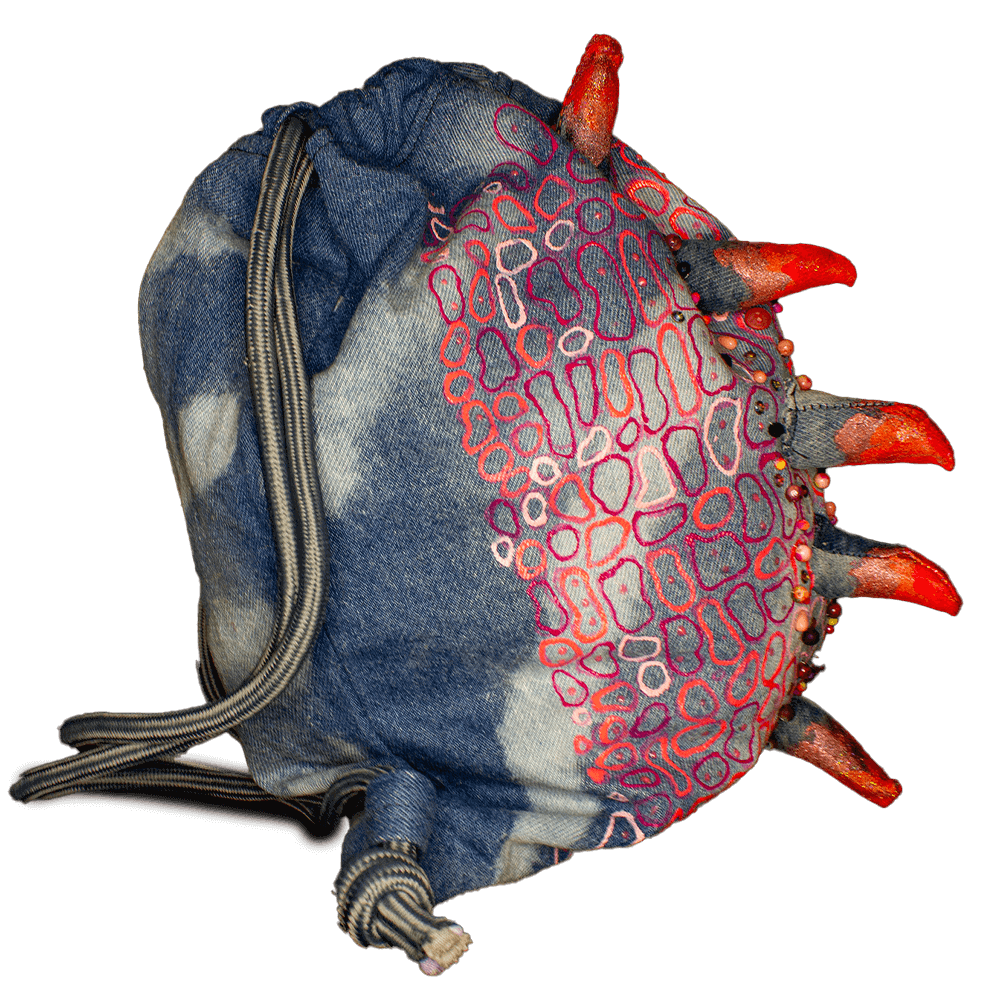 Right side view of the Pink Iguana denim drawstring decorated with a crest made of denim scraps, embroidered decorative beads, 3D paint, resin bones accessories, letter beads, bleach denim effect and fabric paint