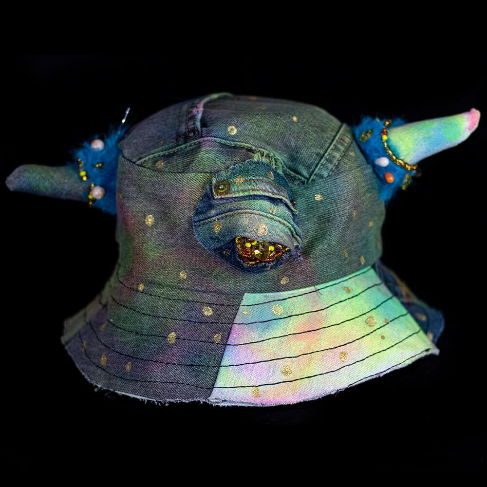 Front view of the MXD Blue bucket hat made from upcycled denim scrap, spray paint texture, golden paint dots, with furry accents on the denim horns and a Cyclop beaded eye