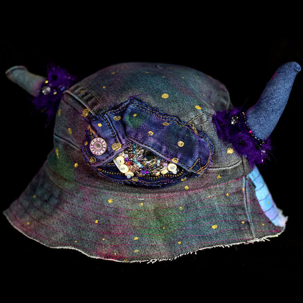 Front view of the MXD Purple bucket hat made from upcycled denim scrap, spray paint texture, golden paint dots, with furry accents on the denim horns and a Cyclop beaded eye