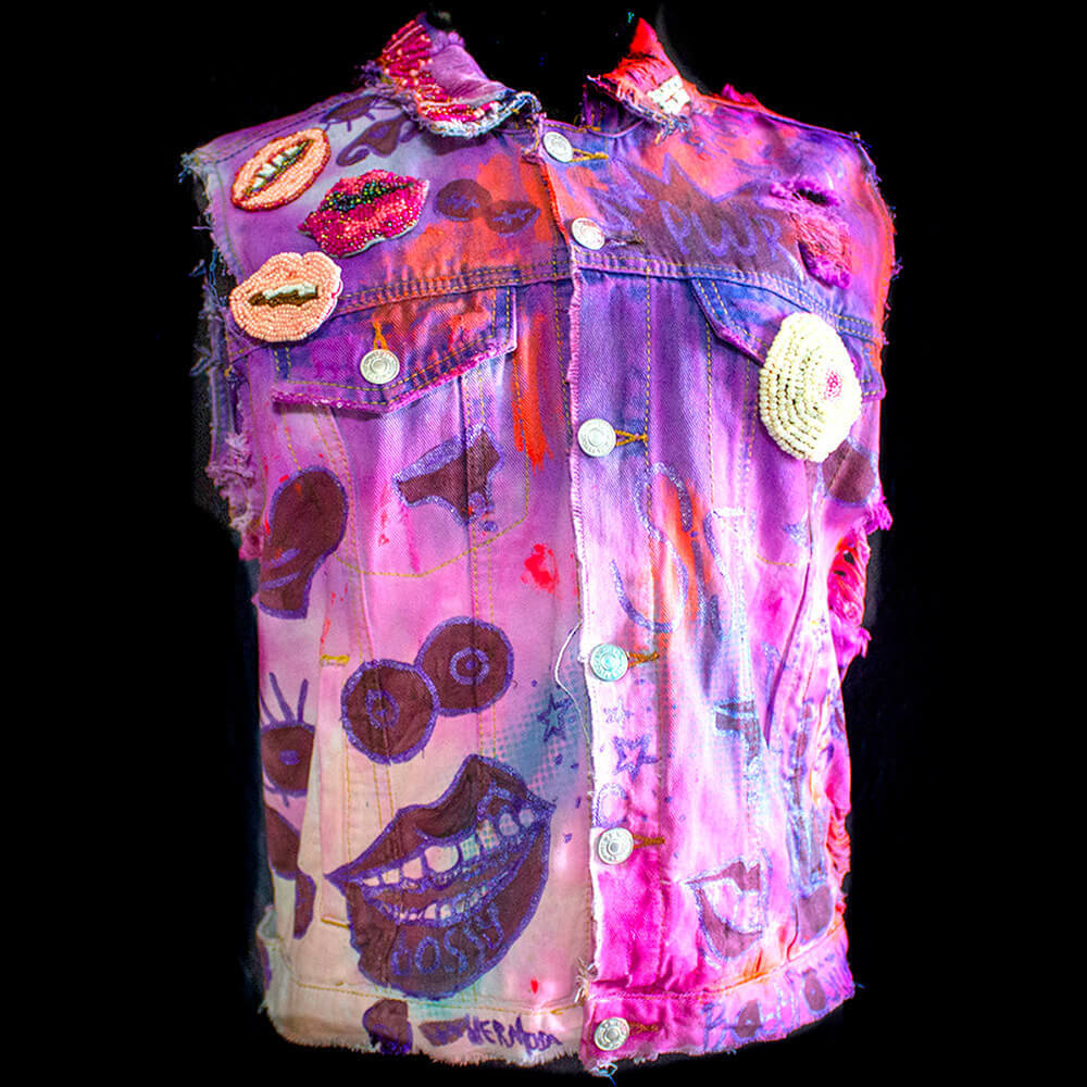 Front view of the Poderosa denim vest decorated with normal fabric paint, iridicent fabric paint and a pink tie dye process., embroidered round beads, letter beads details on collar and 4 removable beaded patches.