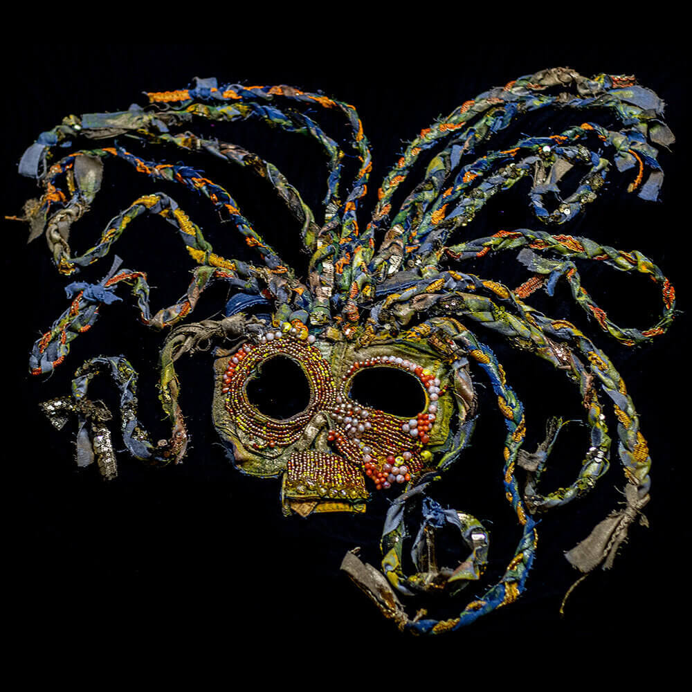 General front view of the Sun - Inti upcycled denim mask decorated with golden and orange beads, decorative braid trim with jean scraps as dreads, fabric paint and 3D paint details