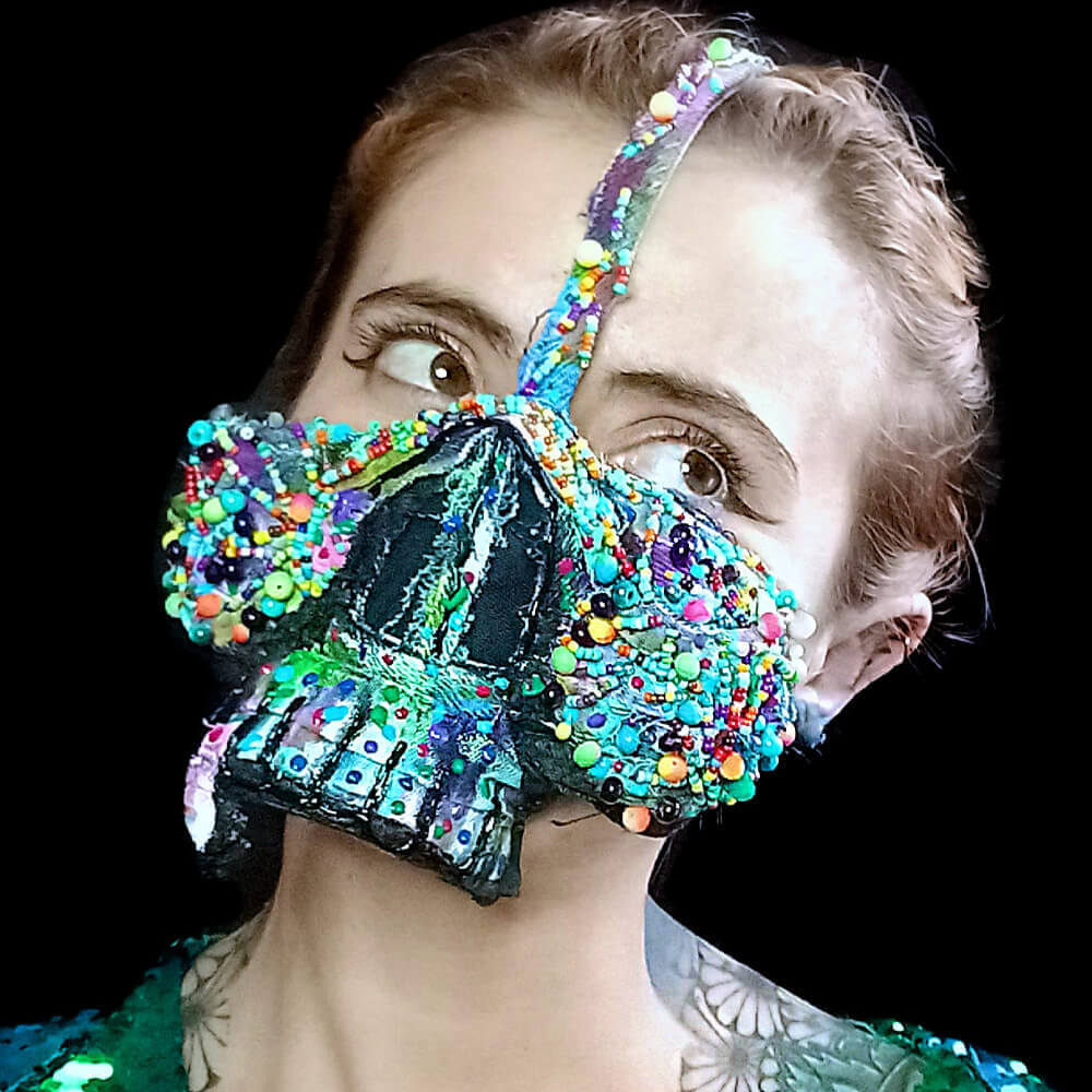 Front view of a model wearing the Dua Tua Skull denim mask crafted from jeans scraps, vibrant multi-colored beads, 3D and regular fabric paint.