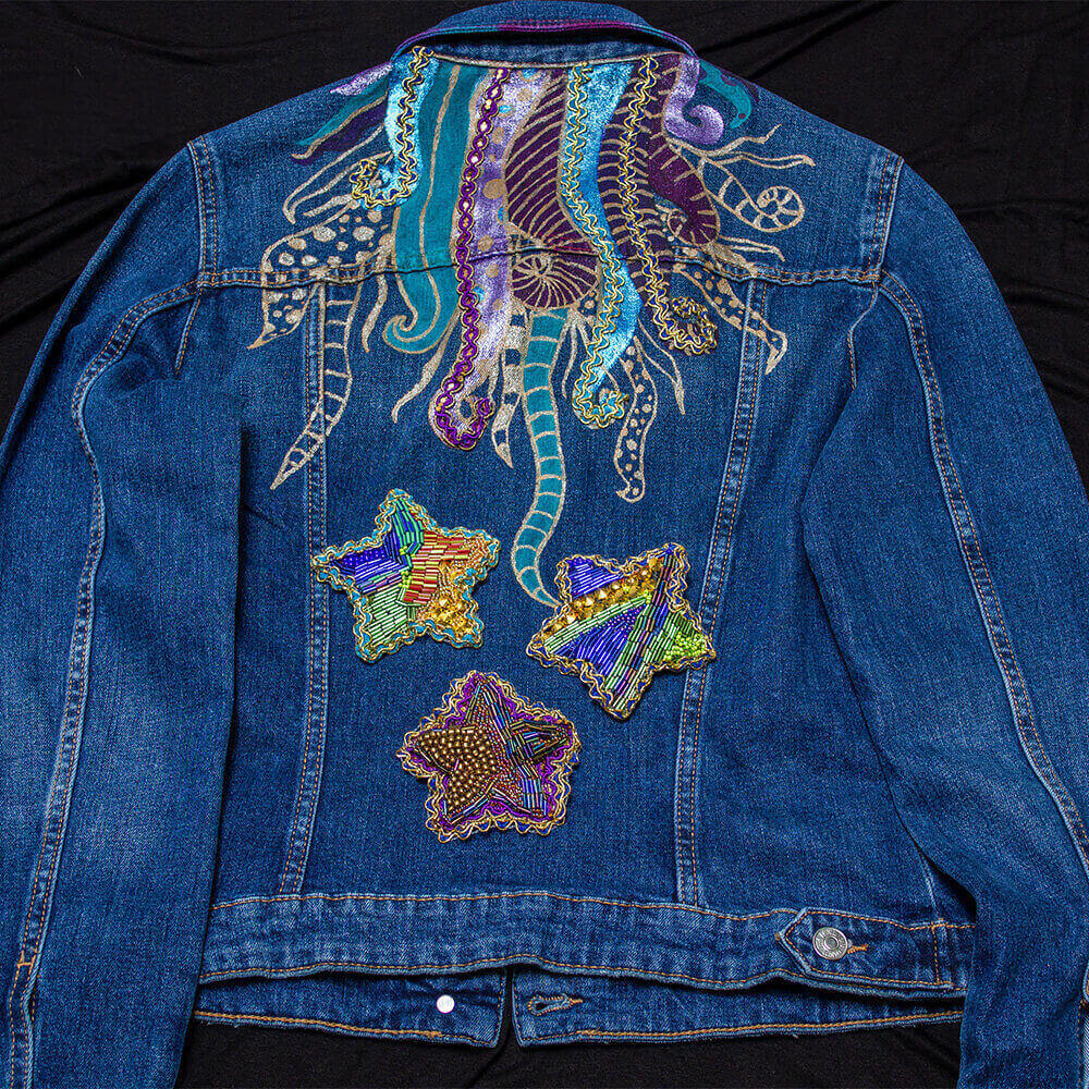 Back view of the Ursula denim jacket customized with metallic painted tentacles, lace details, and fabric paint for the collar color details and 3 removable and beaded star patches