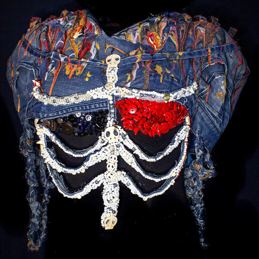 Front view of the Heart Ribs blouse made from upcycled denim, embroidered heart and ribs shape with different accessories like beads, red, black and white buttons, skulls, decorative studs and fabric paint - decorated with denim scraps braids.