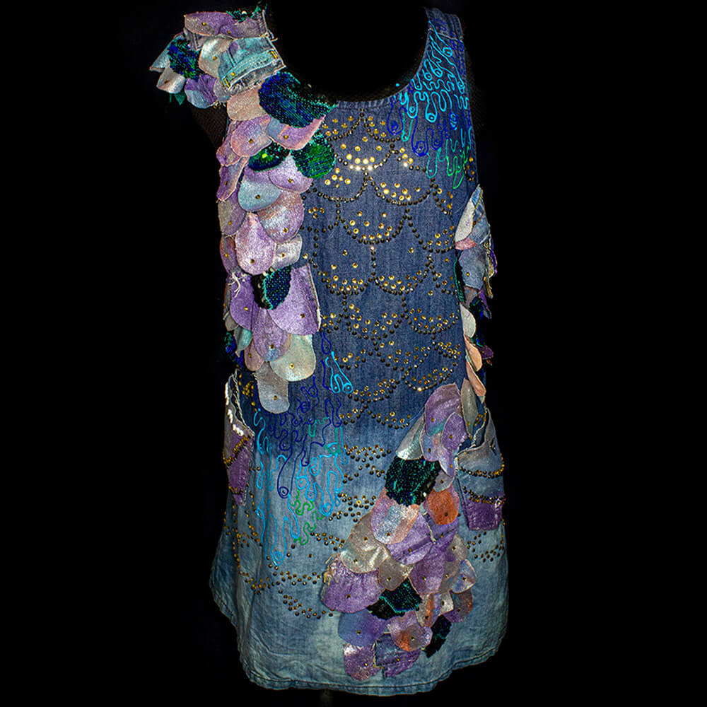 General front view of the of the Escamas denim dress made with scraps of recycled denim and sequins fabric cut into flake shapes decorated with different fabric paint colors and bright fake crystal beads