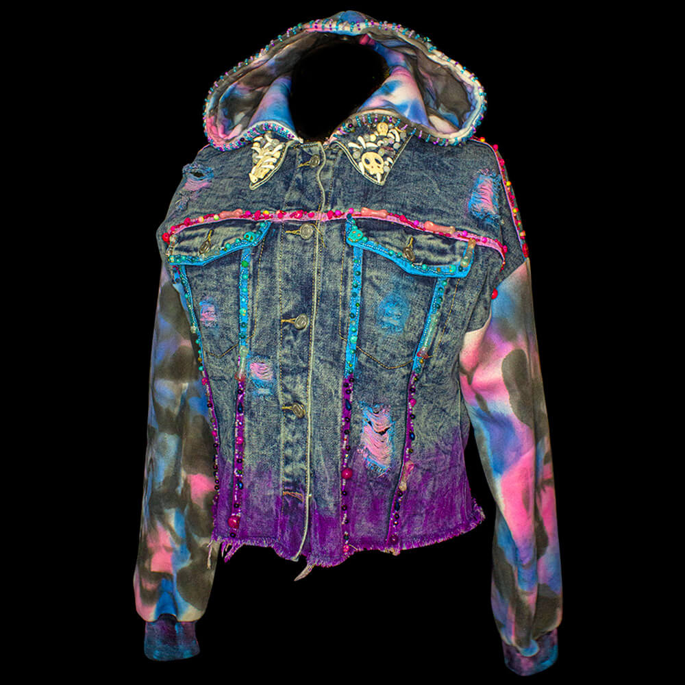 Front view of the Lines-Tie Dye hooded denim jacket decorated with fabric paint, 3D paint, tie dye decoration on the sleeves and hood, reused buttons, resin bones accessories, embroidered beads details on the strips, hood and decorative skulls